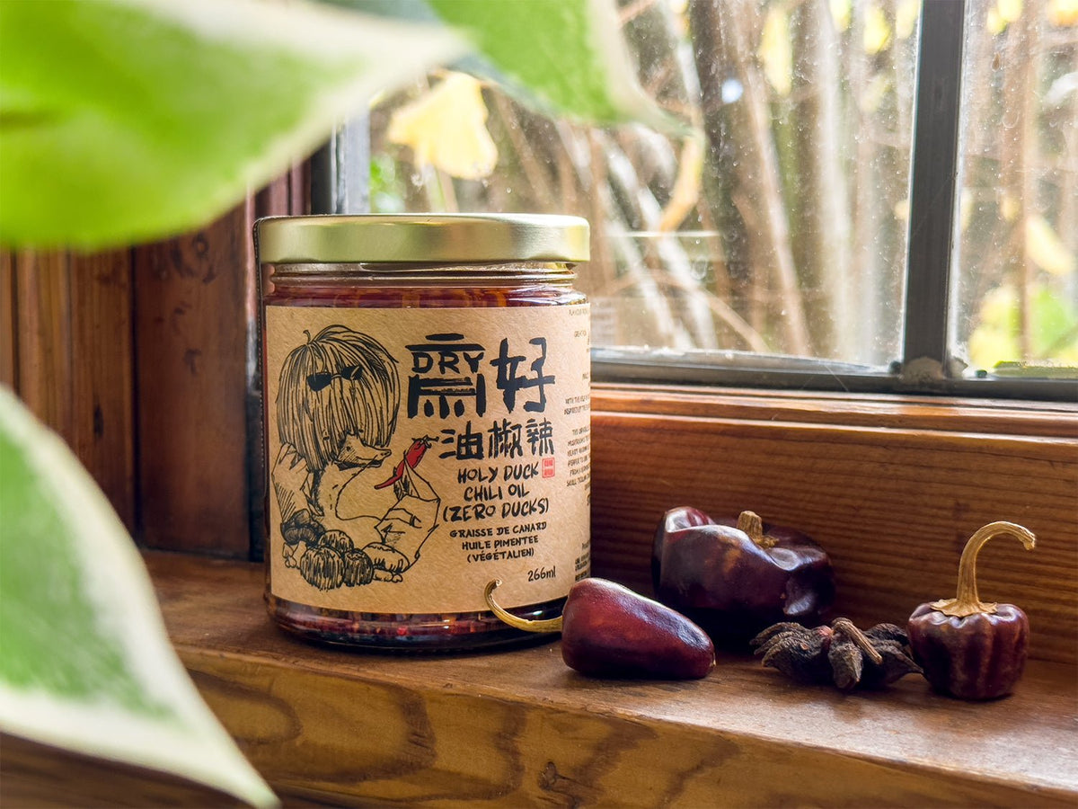 Holy Duck Zero Ducks vegan chili oil on wooden windowsill with dried chilies and autumn foliage — plant-based.